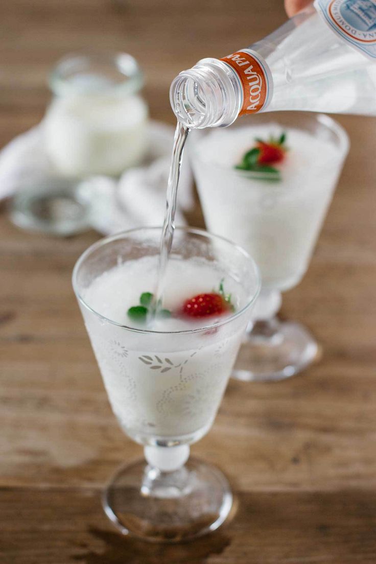 someone is pouring something into a glass filled with ice and strawberries