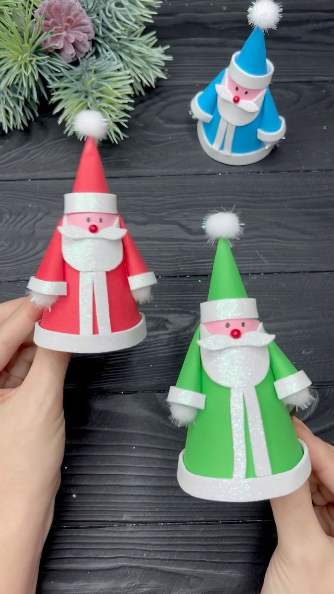 three paper santa hats are being held up by someone's hands on a table