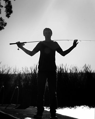 a man holding two fishing rods over his head while standing in front of a body of water