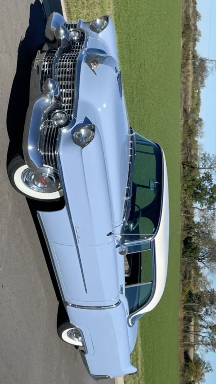 an old blue car parked on the side of the road in front of a grassy field