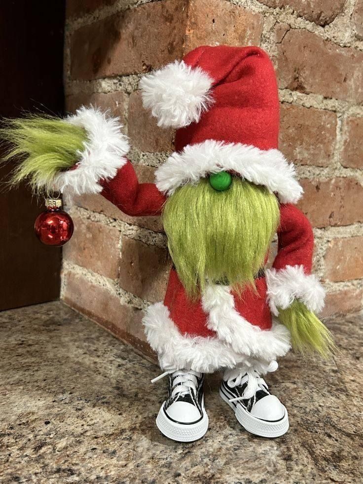 a green and white elf doll standing next to a brick wall