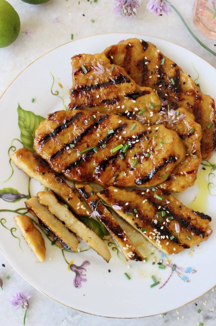 grilled chicken on a white plate with green garnish and purple flowers next to it