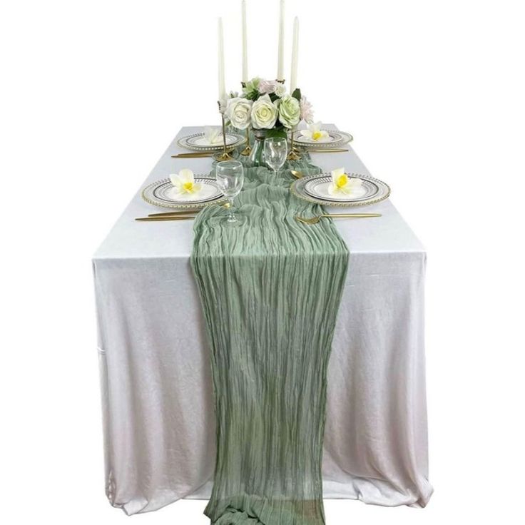 the table is set with white flowers and green linens, gold place settings and silverware