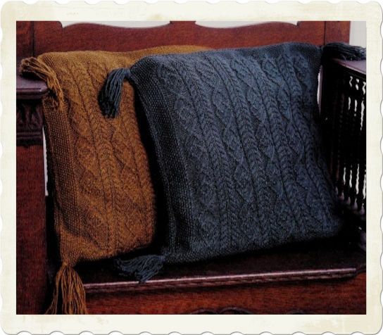 two knitted pillows sitting on top of a wooden bench