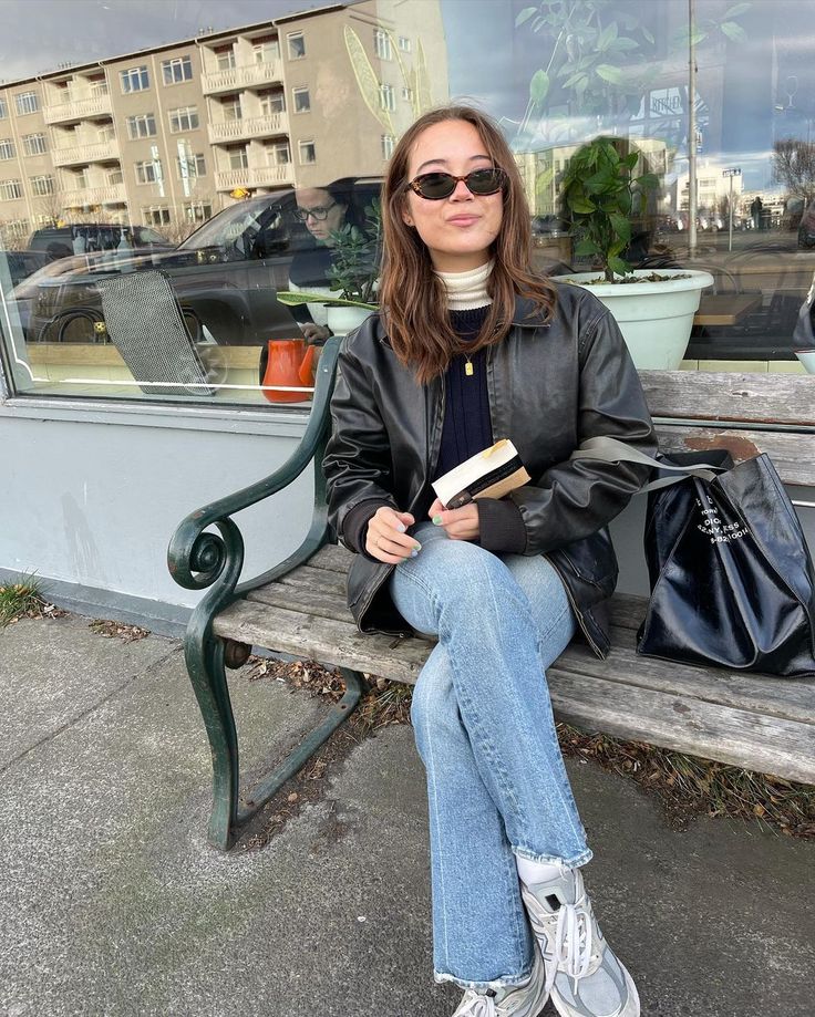 a woman sitting on a bench reading a book in front of a storefront window