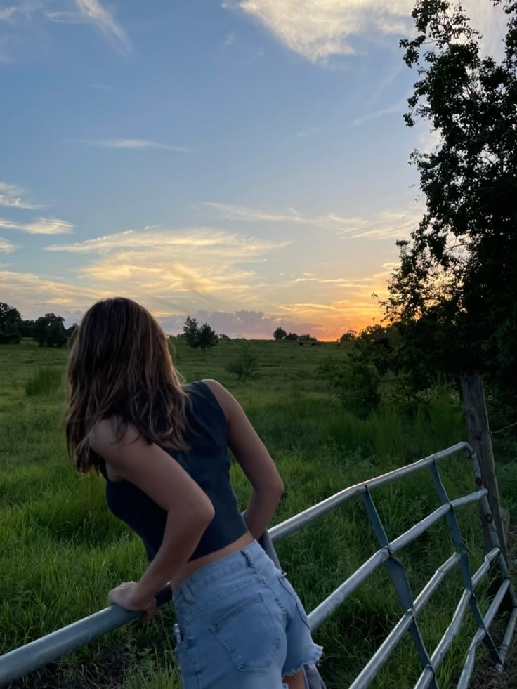 a woman leaning on a fence looking at the sunset