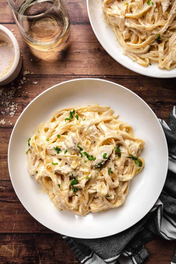 two white plates filled with pasta and garnished with parsley