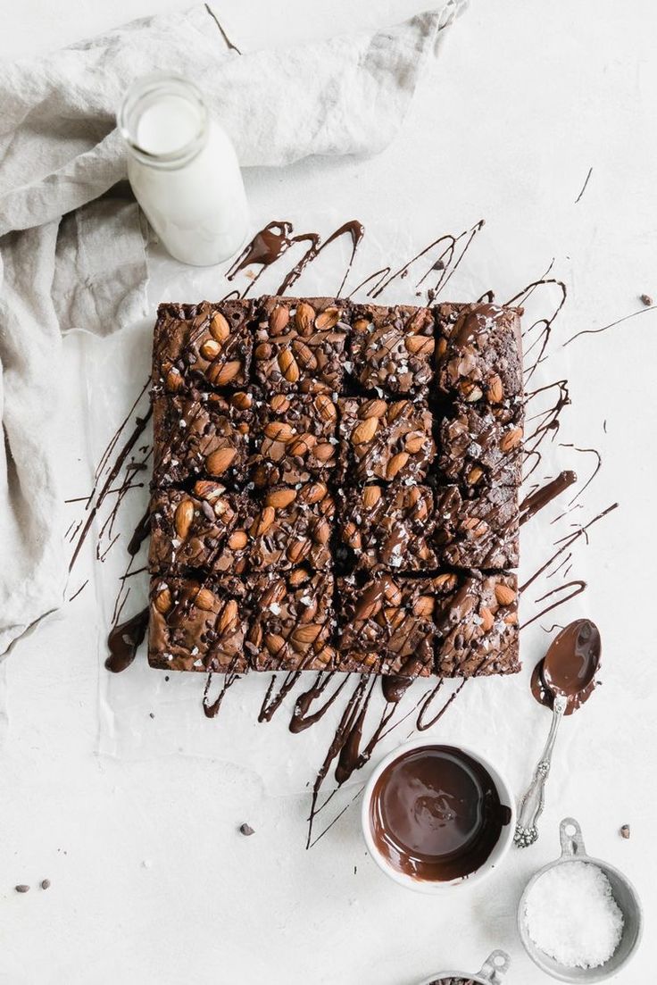 chocolate brownies drizzled with melted chocolate and nuts on a white surface