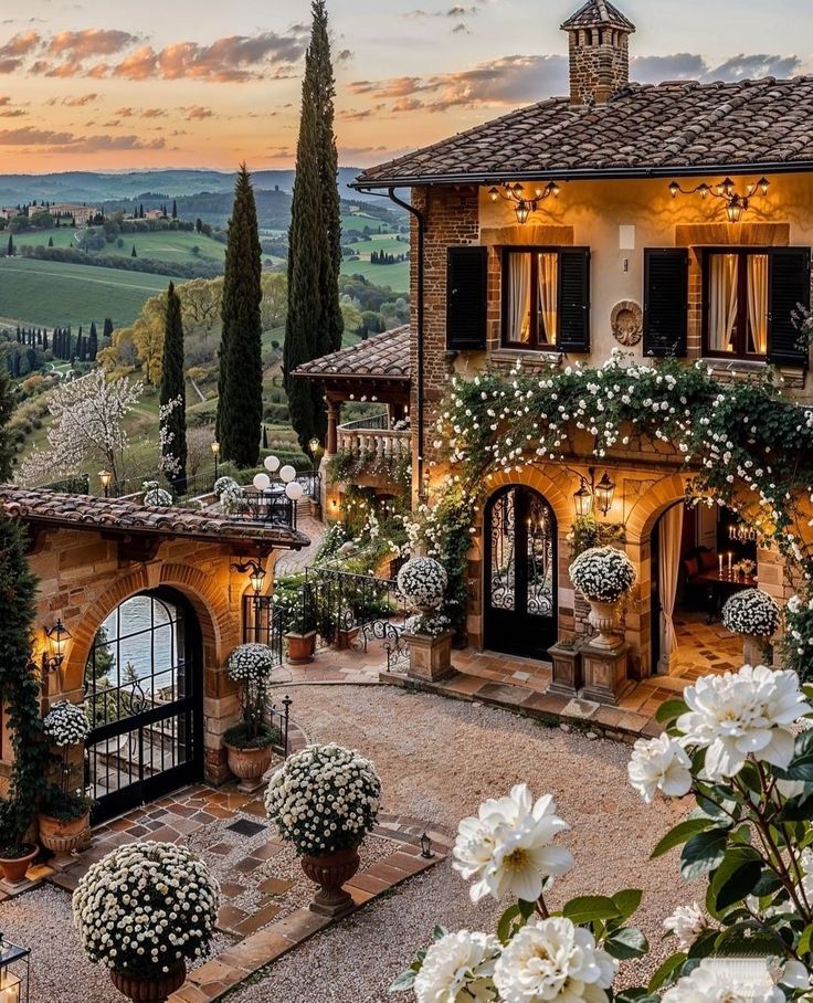 a house with lots of flowers and greenery in front of it at sunset or dawn