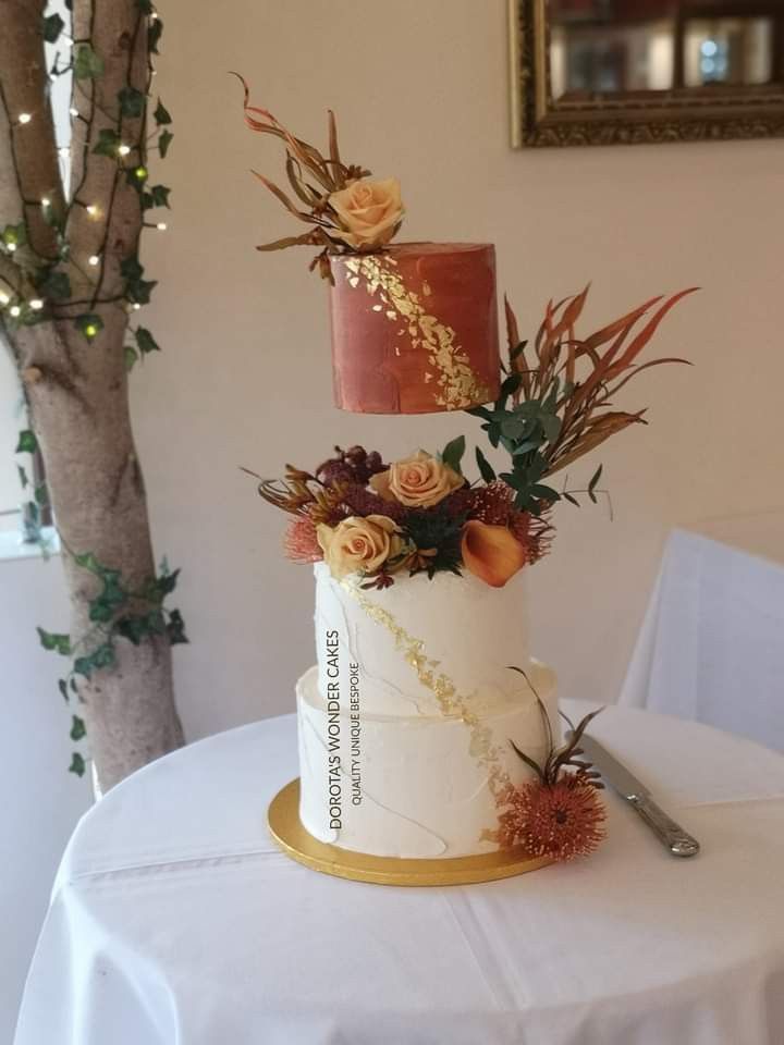 a three tiered wedding cake with flowers and foliage on top, sitting on a table in front of a mirror