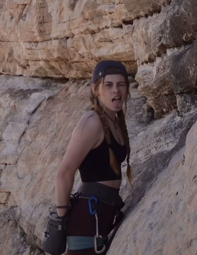 a woman climbing up the side of a mountain with her hands in her pockets and wearing safety gear