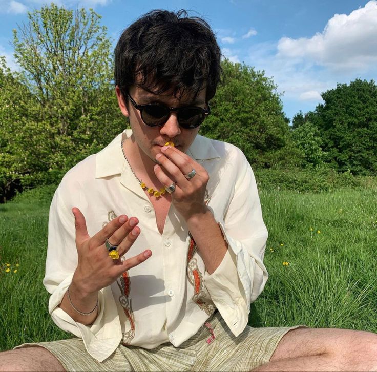 a man sitting in the grass with his fingers crossed and holding something up to his mouth