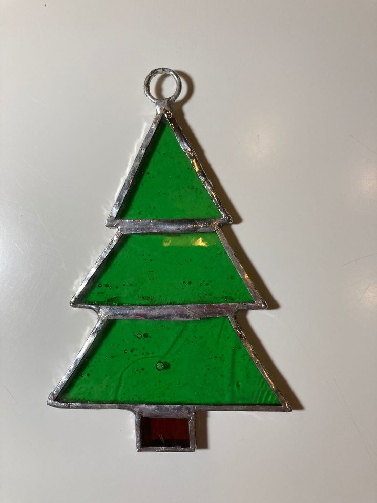 a green glass christmas tree ornament hanging from a hook on a white wall