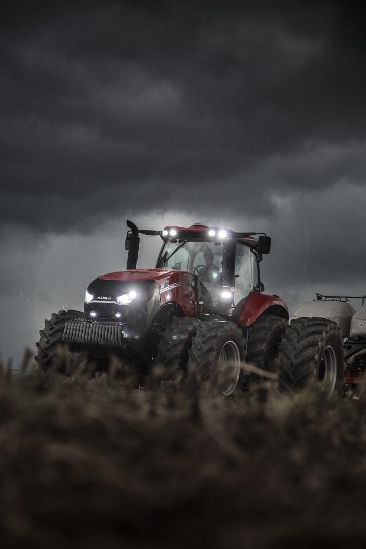 a tractor with lights on driving through a field in the dark storm clouds above it