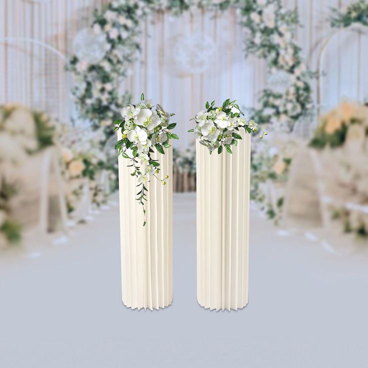 two tall white vases with flowers on them in front of a wedding ceremony setup