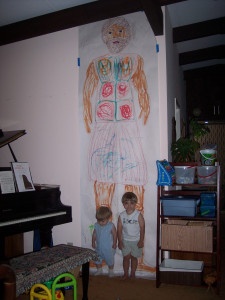 two children standing in front of a drawing on the wall