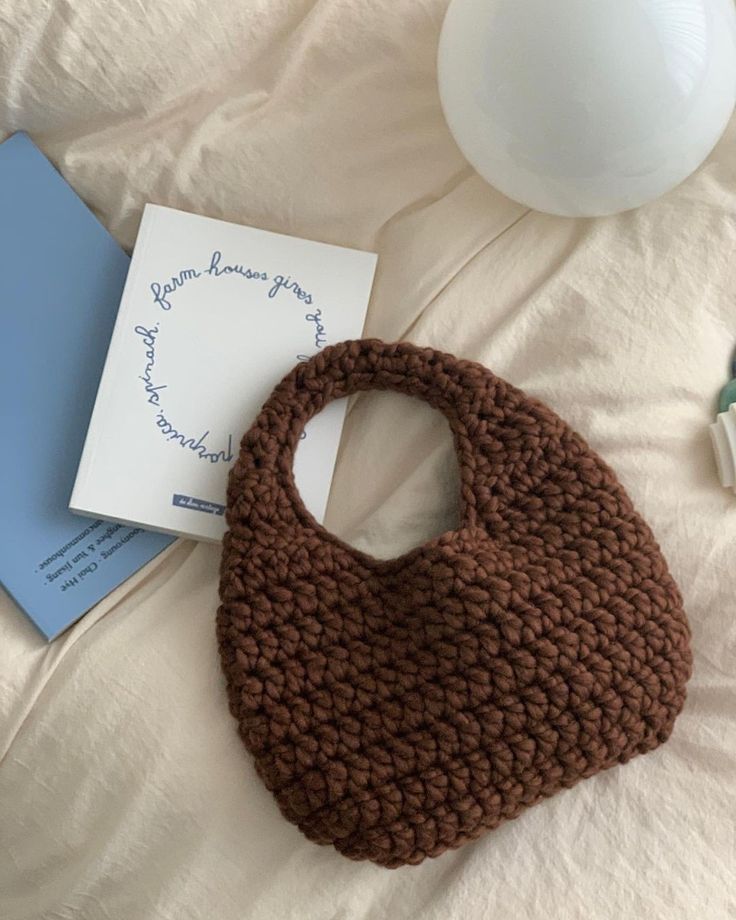 a crocheted purse sitting on top of a bed next to a notepad