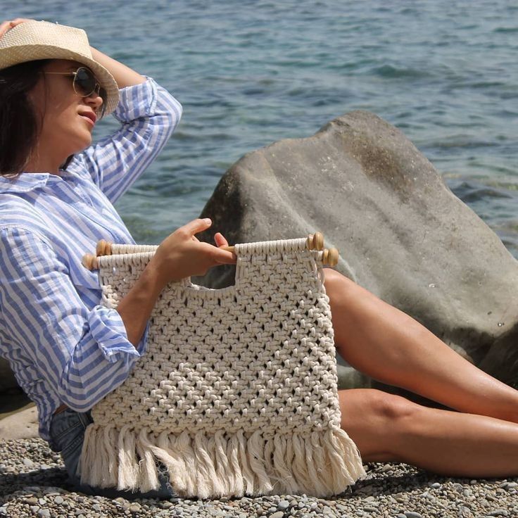 a woman sitting on the beach with a straw bag