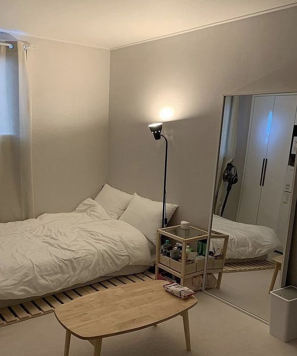 a small bedroom with a bed, mirror and table in the corner next to it