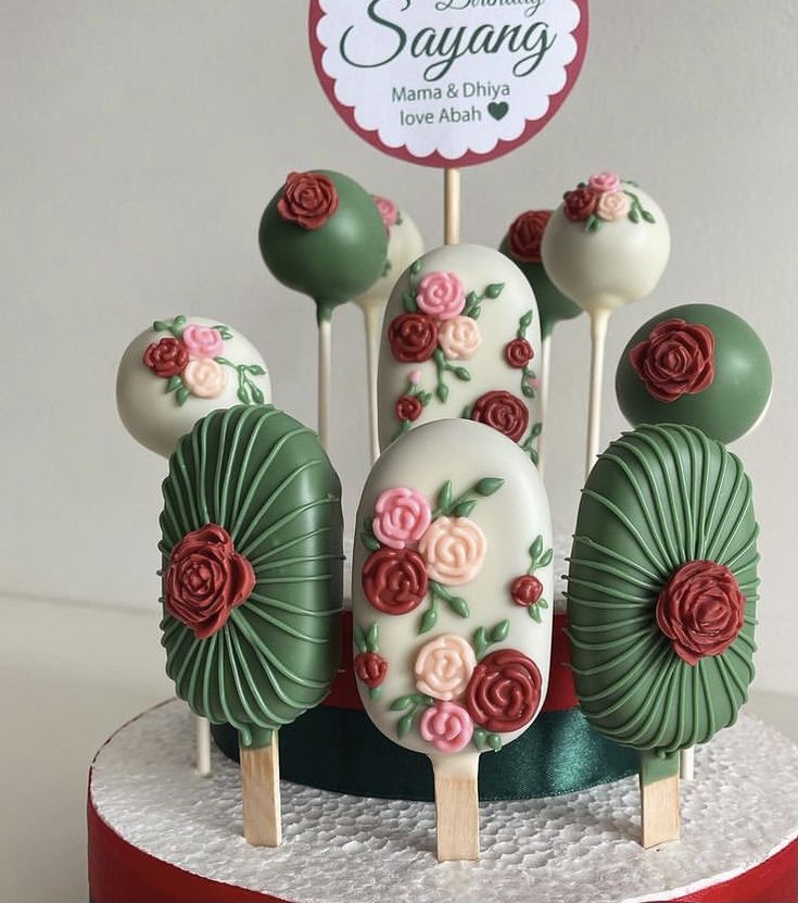 cake pops decorated with flowers and leaves on top of a red stand in front of a happy birthday sign