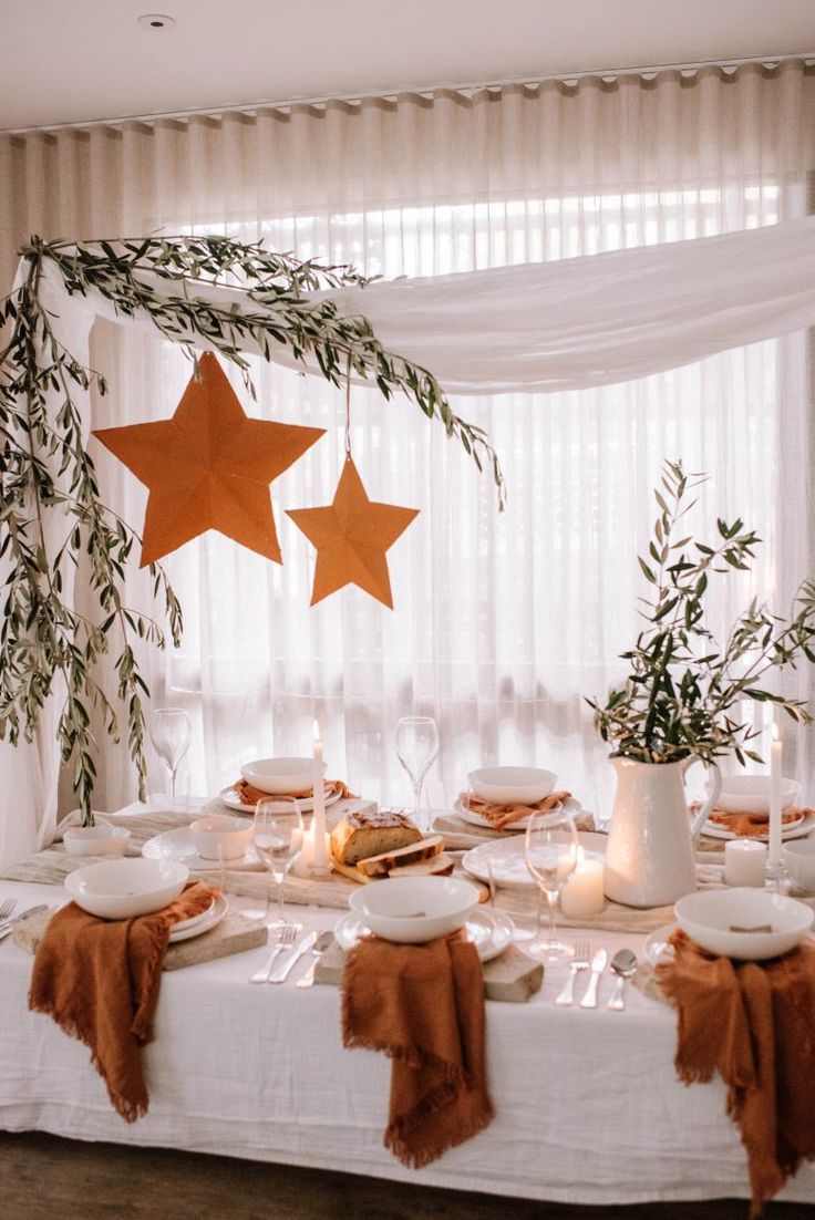 the table is set with white plates and brown napkins, two stars hanging from the ceiling