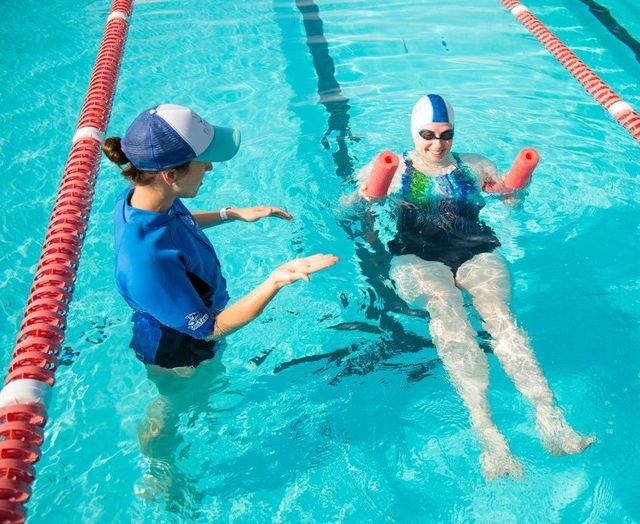 two people are swimming in the pool and one person is pointing to something on his arm