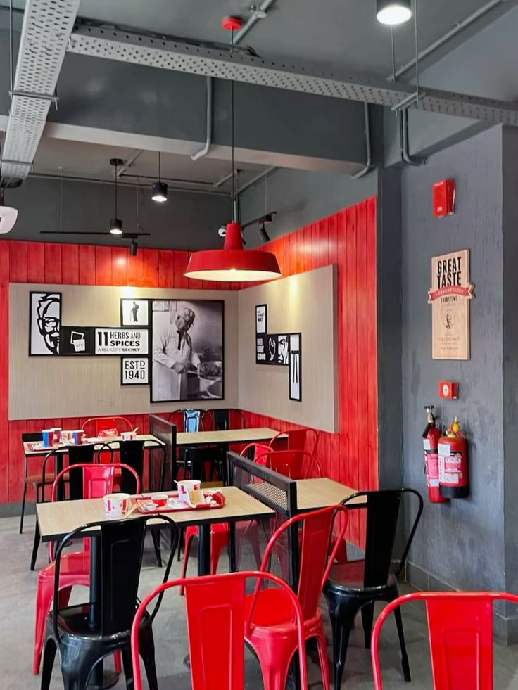 the interior of a restaurant with red chairs and black tables in front of a gray wall