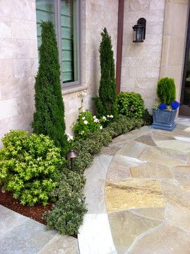 an outdoor area with stone walkways and plants on the side of the house,