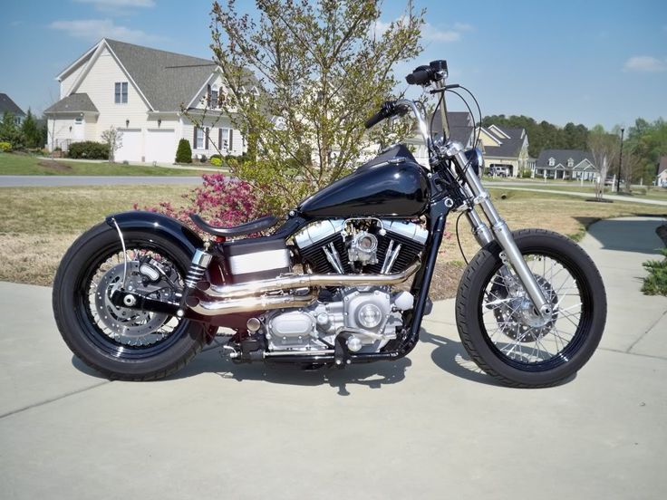 a black motorcycle parked on top of a cement lot next to a tree and house