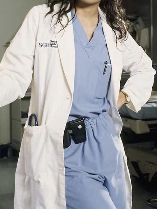 a woman in a white lab coat and blue scrubs is posing for the camera