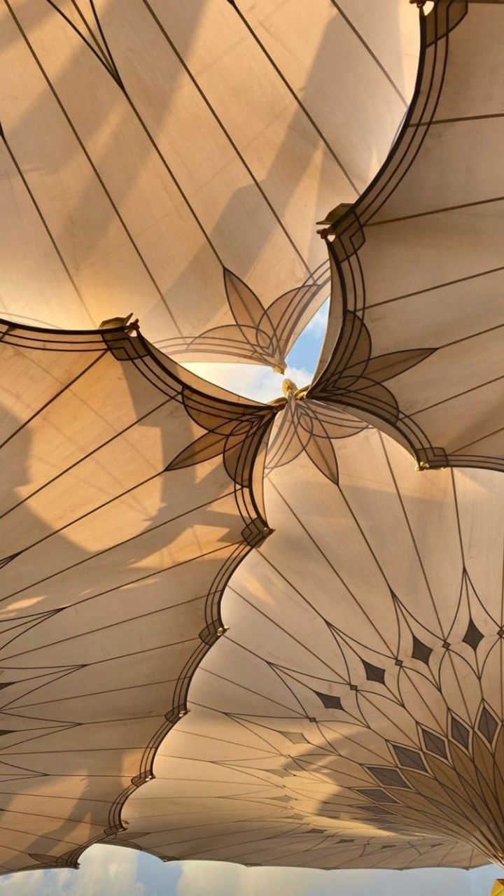 several large umbrellas are hanging from the ceiling in an open air area with blue sky and clouds behind them