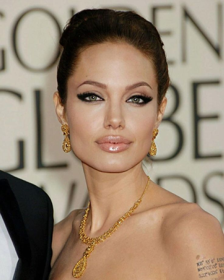 a woman in a black suit and gold jewelry on the red carpet at an awards event