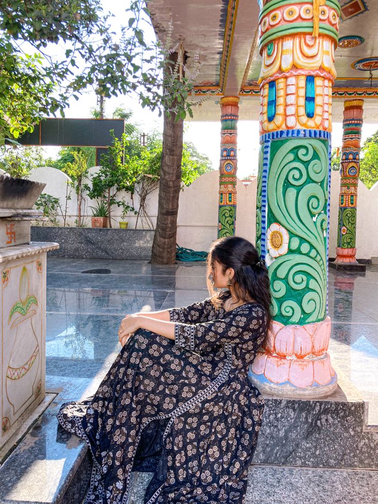 a woman sitting on the ground in front of a pillar with an intricate design and colorful columns