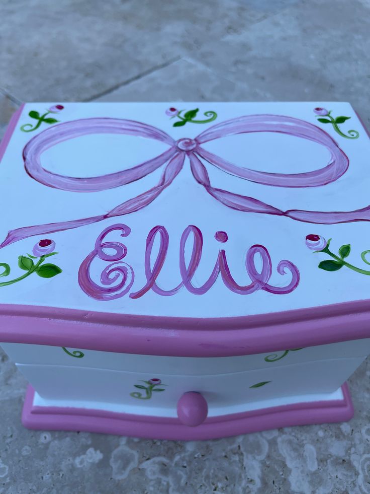 a pink and white box with a bow on the lid that says,'ellie '