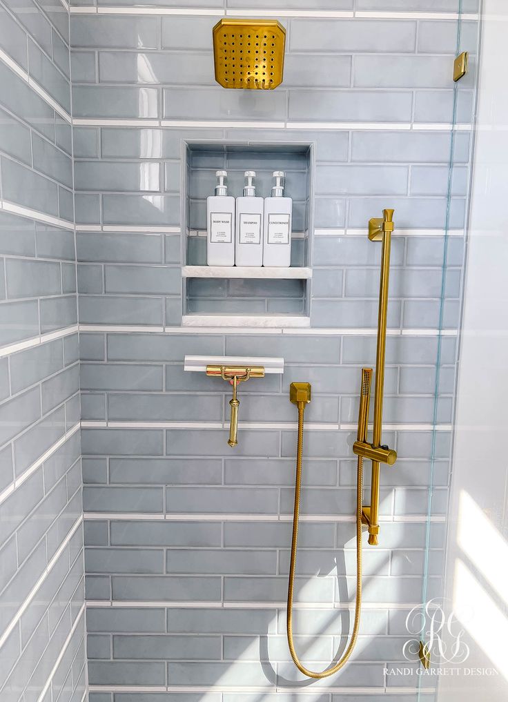 a white and gold tiled bathroom with shower head, soap dispenser, and shelves