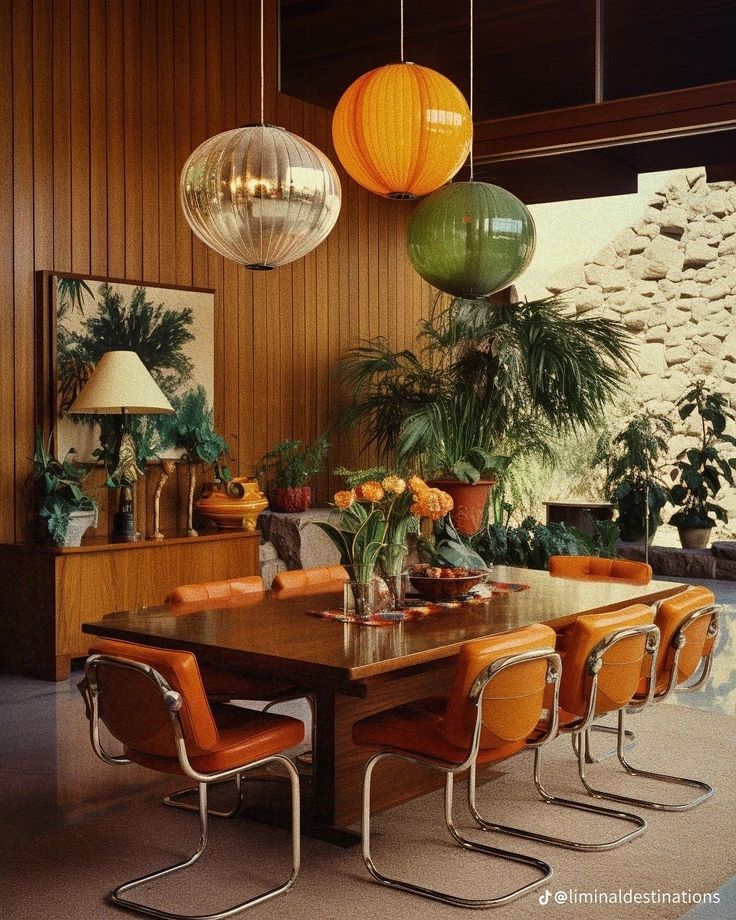 a dining room table surrounded by orange chairs and hanging lights over it's head