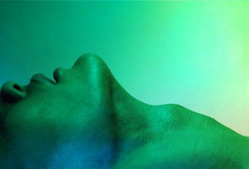 a man laying down with his eyes closed in front of a green and blue background