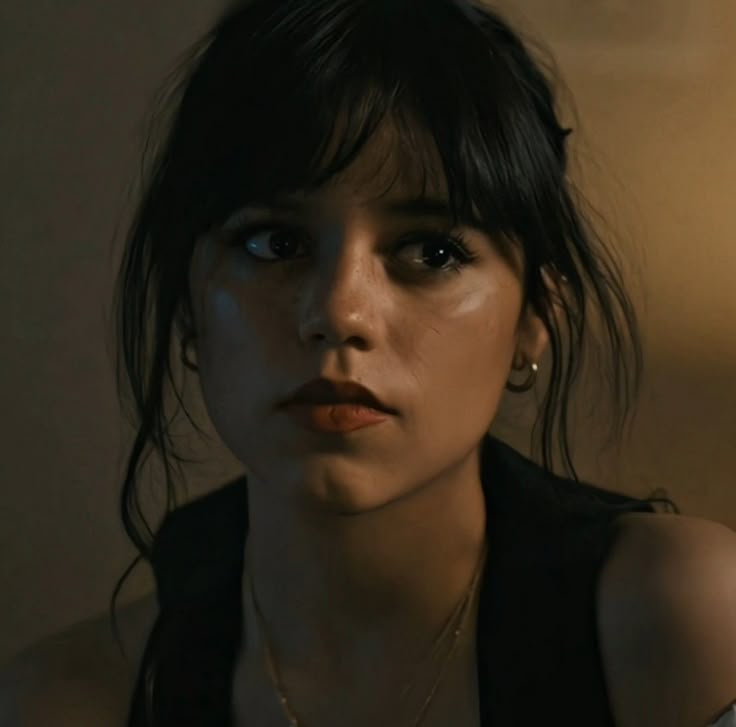 a close up of a person wearing a necklace and looking at the camera with an intense look on her face