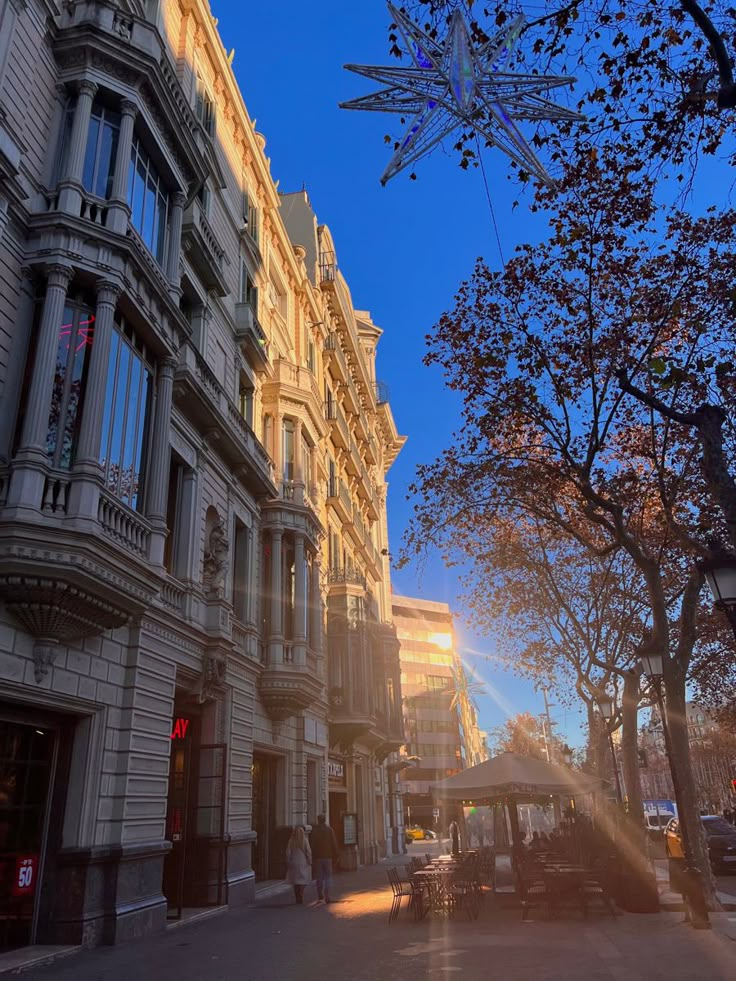 the sun shines brightly in front of buildings on a street with trees and people walking