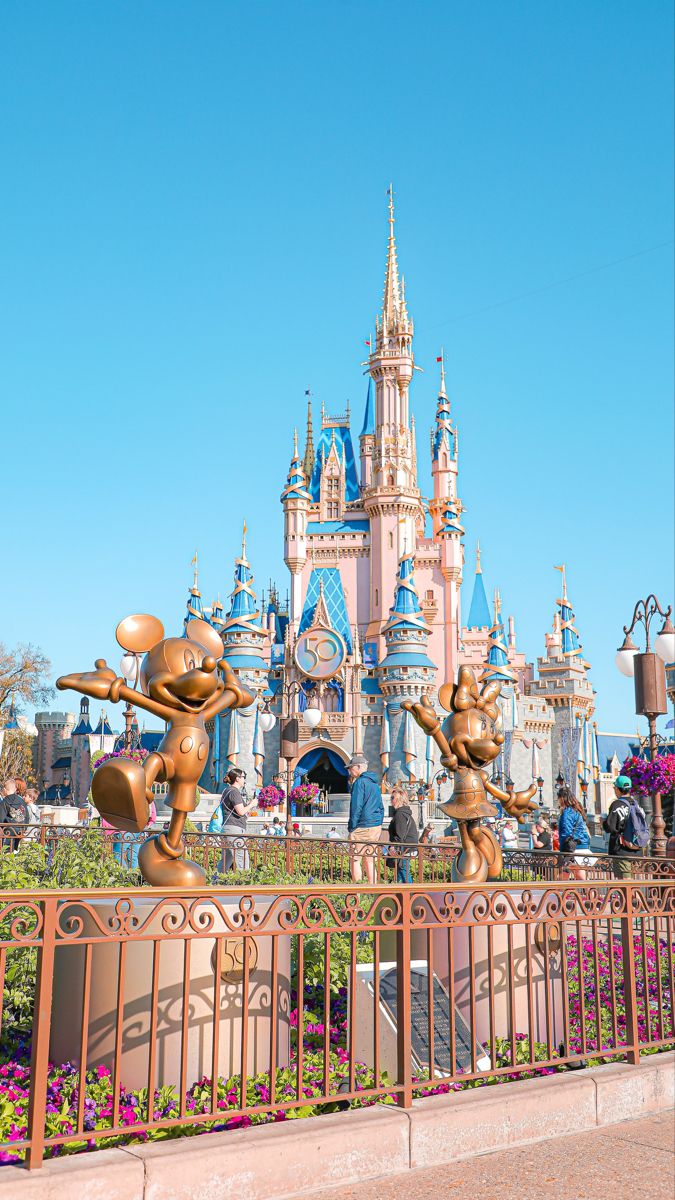 the entrance to disneyland's castle is decorated with gold mickey mouse statues and pink flowers