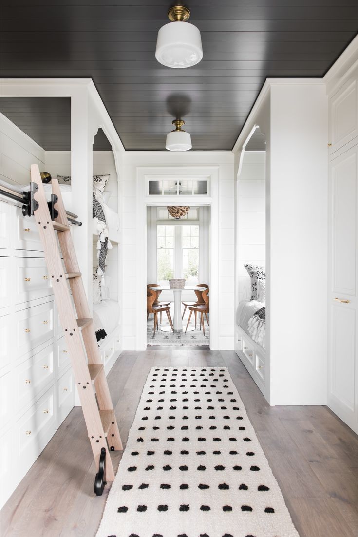 a white hallway with black and white rugs on the floor next to a ladder