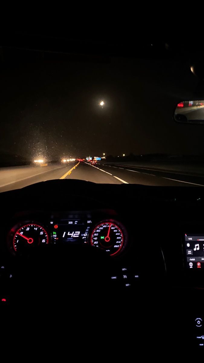 the dashboard of a car at night with lights on and fog in the air behind it