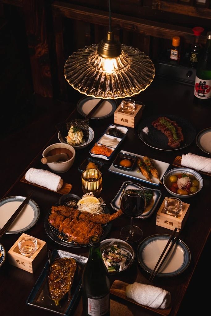 a table topped with lots of plates and bowls filled with food next to a bottle of wine