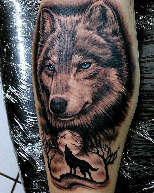 a wolf tattoo on the leg with blue eyes and an image of a wolf in the background