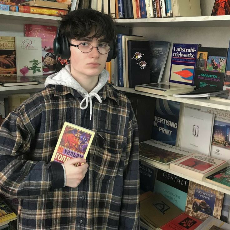 a boy wearing headphones and holding a book in front of bookshelves full of books