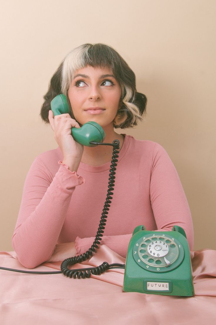 a woman sitting on a bed while talking on a green phone with her eyes closed