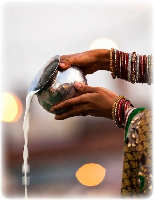 a woman is pouring water from a metal bowl into her hand and holding it with both hands