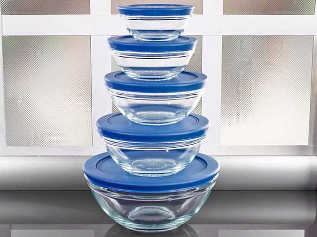 four glass bowls stacked on top of each other in front of a window with blue lids