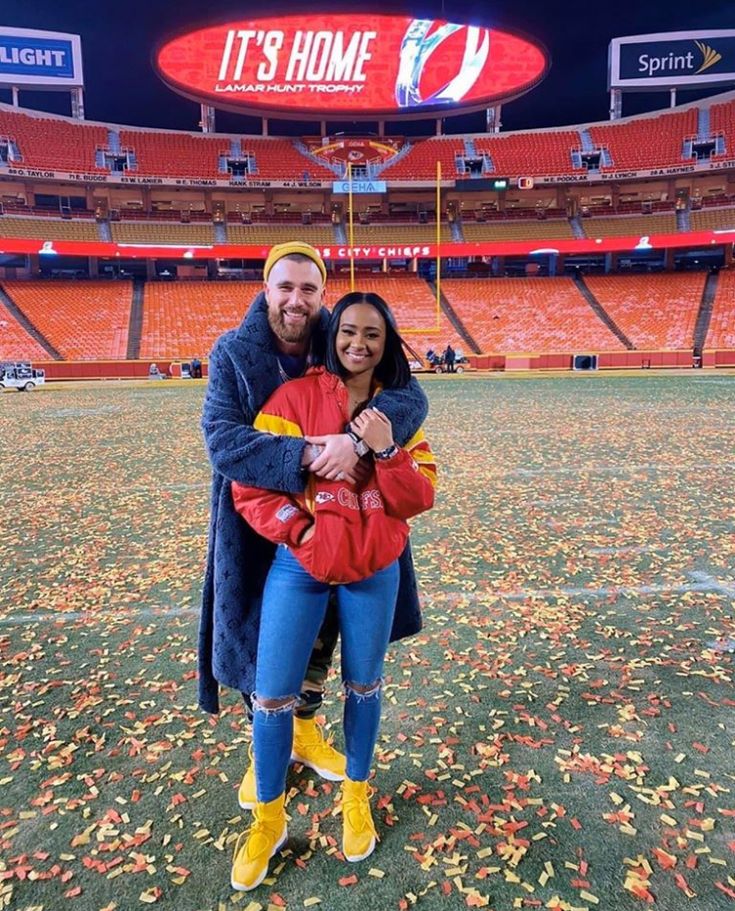 a man and woman posing for a photo in front of an empty football stadium at night