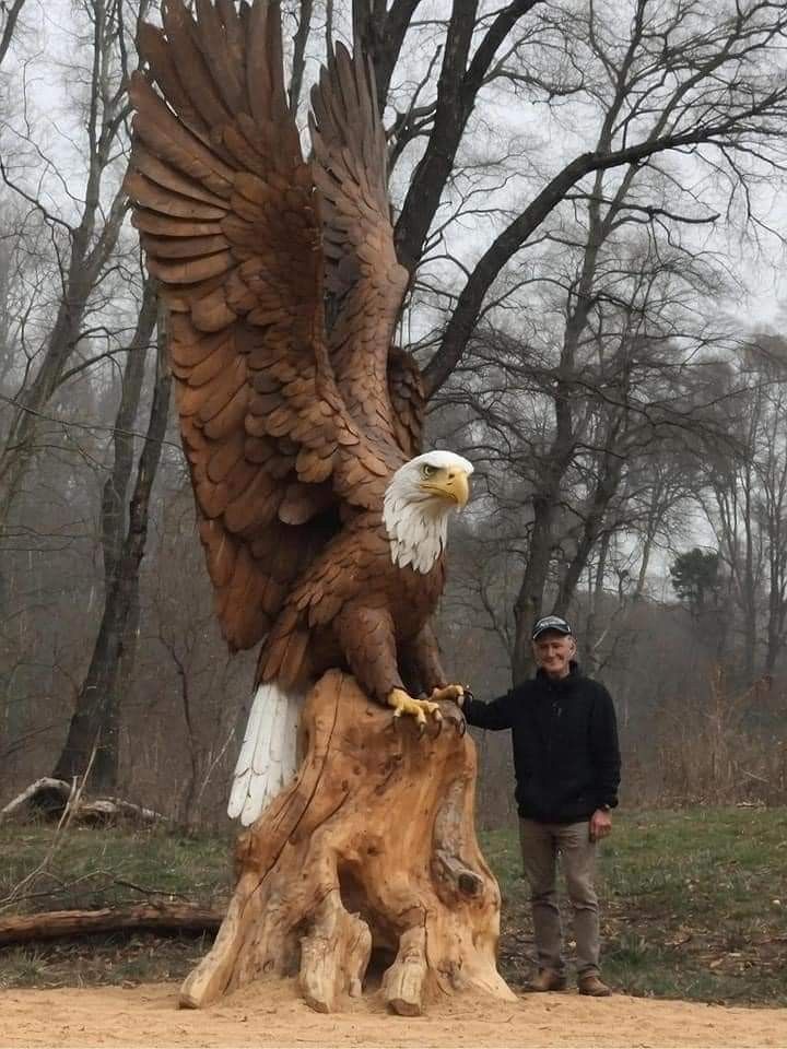 a man standing next to a statue of an eagle on top of a tree stump